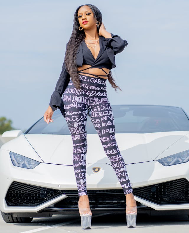 A lady wearing Dolce & Gabbana clothing, stood by a sports car.