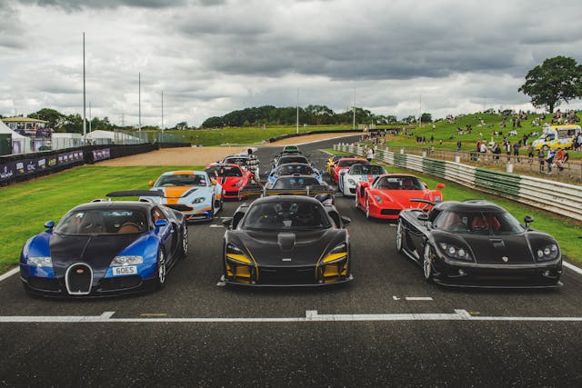 Several luxury sports cars, including a Bugatti, lined up on a race-track starting grid.